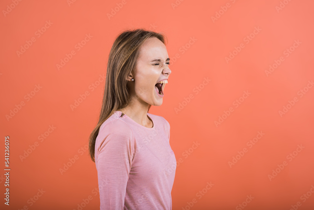An aggressive girl frowns, she is aggressive, she is stressed and screams on a red background. An aggressive girl frowns, she is aggressive, she is stressed and screams on a red background.