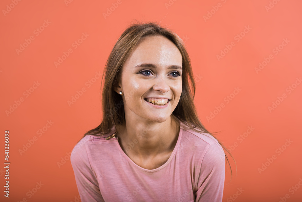 Close-up portrait of a happy Caucasian girl in a pink jumper who is smiling on a red background. Close-up portrait of a happy Caucasian girl in a pink jumper who is smiling on a red background.