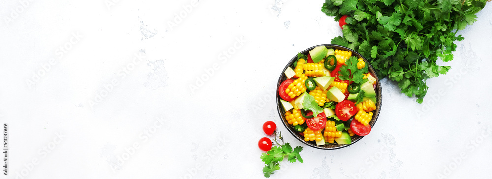 Mexican spicy salad with corn, avocado, jalapeno peppers, cherry tomatoes and cilantro. White kitchen table background, top view banner