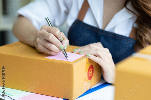 Shipping shopping online, young woman starts up small business owner writing address on cardboard box. Small business entrepreneur SME or freelance Asian woman working with parcel box at home.