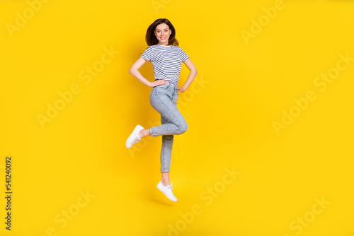 Full body photo of cute young lady hands waist jumping look camera poster wear stylish striped outfit isolated on yellow color background