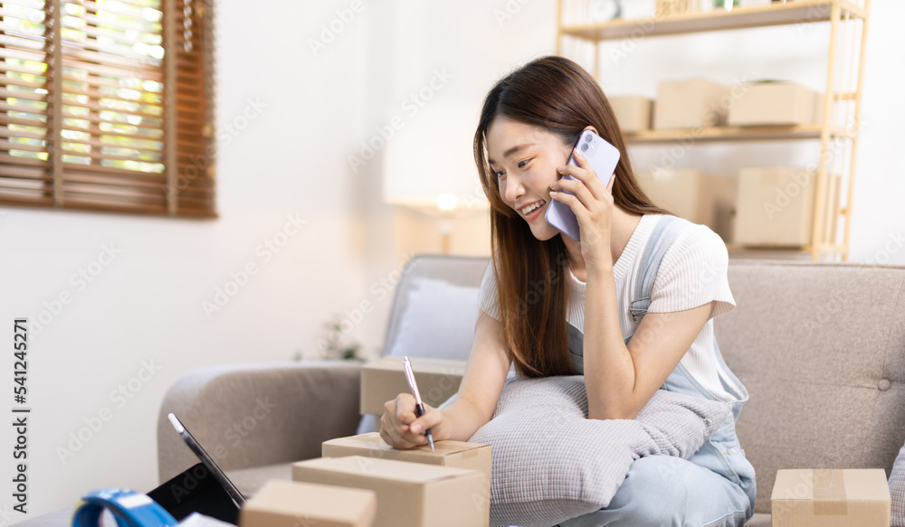 E-commerce businessman is talking on the phone with a customer who comes in to inquire and place her order, Woman writes mailbox address in preparation for delivery, SME entrepreneur, Packing box. E-commerce businessman is talking on the phone with a customer who comes in to inquire and place her order, Woman writes mailbox address in preparation for delivery, SME entrepreneur, Packing box.