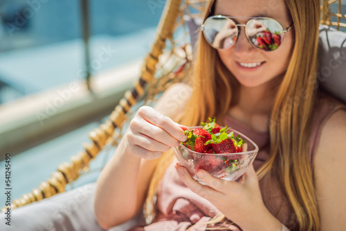 Portrait of gorgeous woman wearing beautiful dress sitting in a patio and eating strawberry