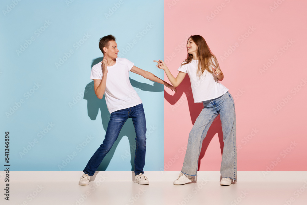 Fototapeta premium Portrait of young couple, man and woman in casual clothes dancing isolated over blue-pink background. Friendship