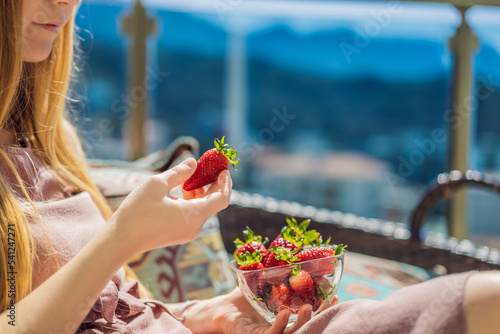 Portrait of gorgeous woman wearing beautiful dress sitting in a patio and eating strawberry © galitskaya