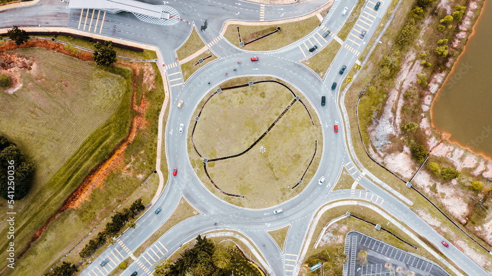 Aerial top down view of traffic roundabout on a main road. Aerial view of roundabout in the city in the summer. Aerial view of traffic infrastructure. Sedan cars moving over the asphalt. Road crossing Aerial top down view of traffic roundabout on a main road. Aerial view of roundabout in the city in the summer. Aerial view of traffic infrastructure. Sedan cars moving over the asphalt. Road crossing