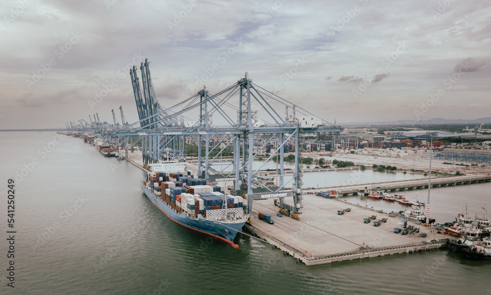Klang, Malaysia - September 25, 2022: Cranes at the port Klang near Kuala Lumpur. Container crane at Klang Harbor. Aerial view on a container ship which is being loaded. Heavy Trucks at the Cargo bay