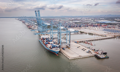 Klang, Malaysia - September 25, 2022: Cranes at the port Klang near Kuala Lumpur. Container crane at Klang Harbor. Aerial view on a container ship which is being loaded. Heavy Trucks at the Cargo bay