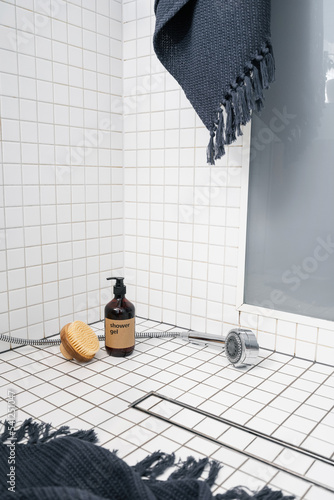 Dispenser bottle with gel and wooden brush on white tiled bathroom floor