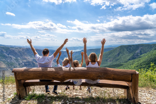 Family is sitting on wooden bench and watching beautiful nature and mountains. Happy family of four sitting on bench by cliff of Sulak canyon in Dagestan. photo