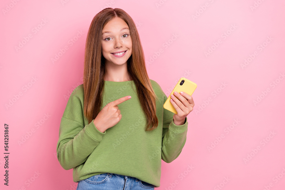 Portrait of positive good mood girl long hairstyle dressed green sweatshirt directing at smartphone isolated on pink color background Portrait of positive good mood girl long hairstyle dressed green sweatshirt directing at smartphone isolated on pink color background