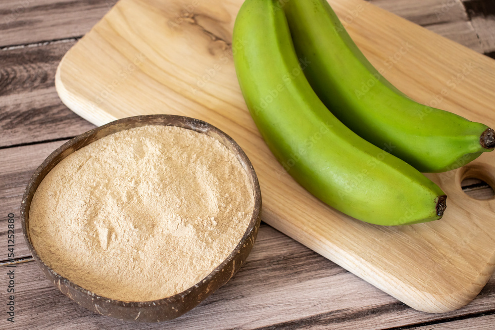 Banana brown flour in a natural bowl on a wooden surface with fresh green bananas Banana brown flour in a natural bowl on a wooden surface with fresh green bananas
