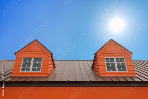 dormer with windows on metal sheet roof with blue sky and sunshine