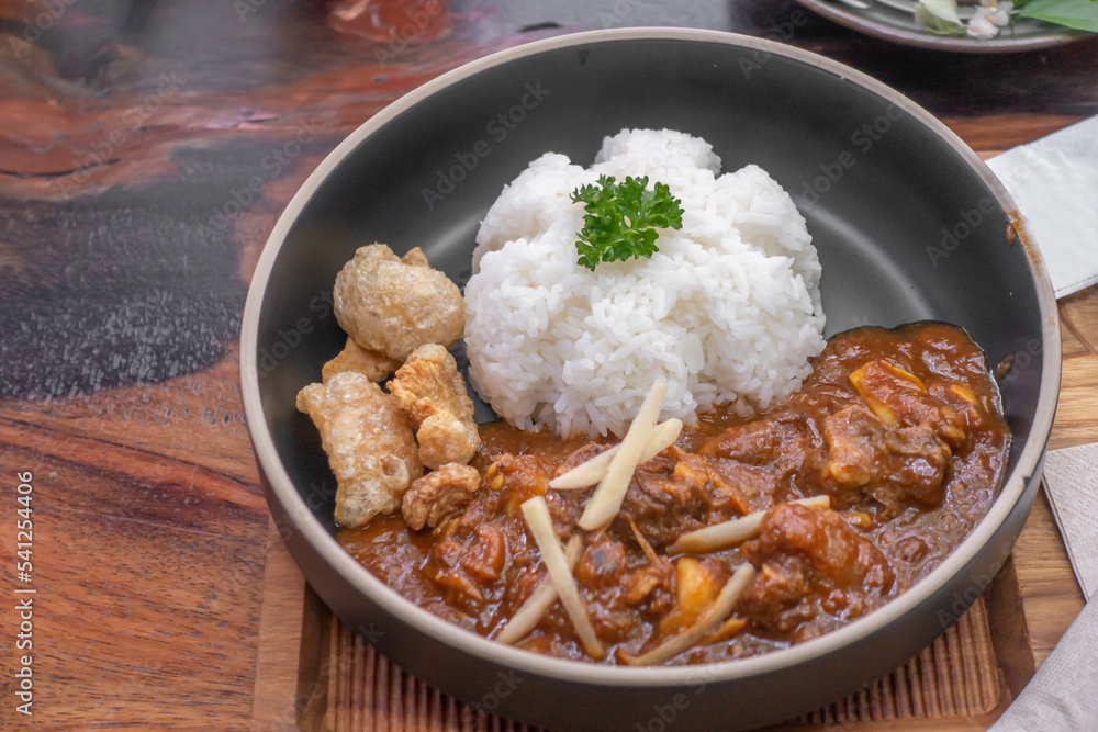 The dish of fried pork or fish with whtie jasmine rice topped by cyrantro with spoon and fork set in restaurant.