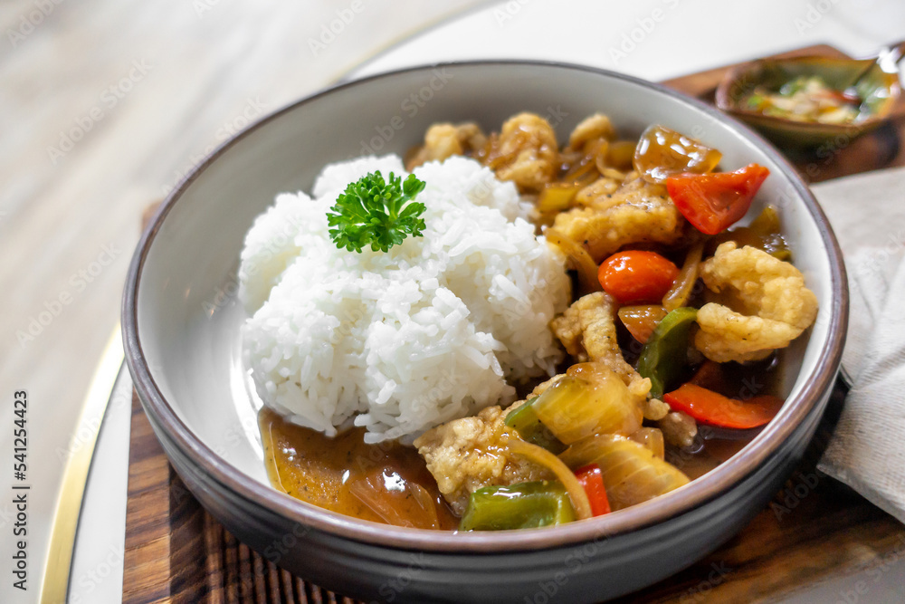 The dish of fried pork or fish with whtie jasmine rice topped by cyrantro with spoon and fork set in restaurant.