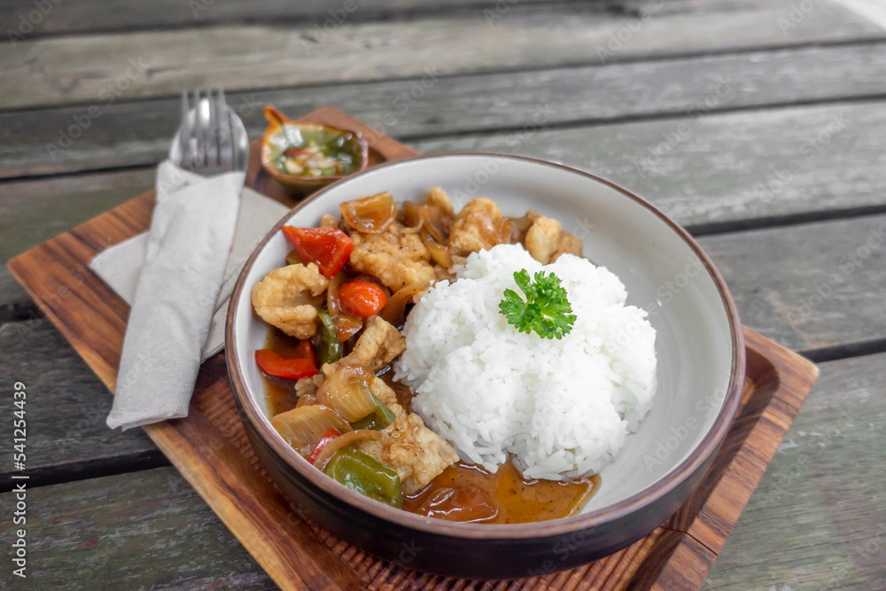The dish of fried pork or fish with whtie jasmine rice topped by cyrantro with spoon and fork set in restaurant.