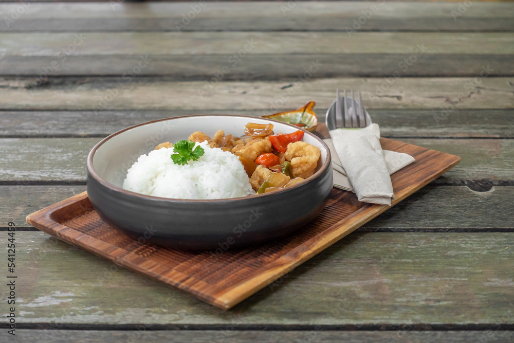 The dish of fried pork or fish with whtie jasmine rice topped by cyrantro with spoon and fork set in restaurant.