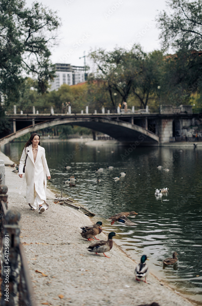 Fototapeta premium Young pretty woman walks in park near lake with ducks.