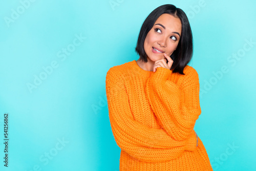 Photo of positive thoughtful woman with straight hairdo dressed orange pullover look empty space isolated on turquoise color background