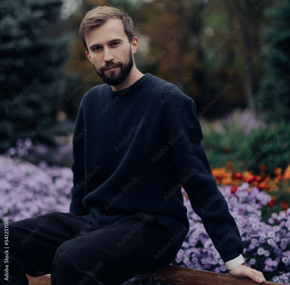 Young happy man rests on bench in park near flowerbed. Young happy man rests on bench in park near flowerbed.