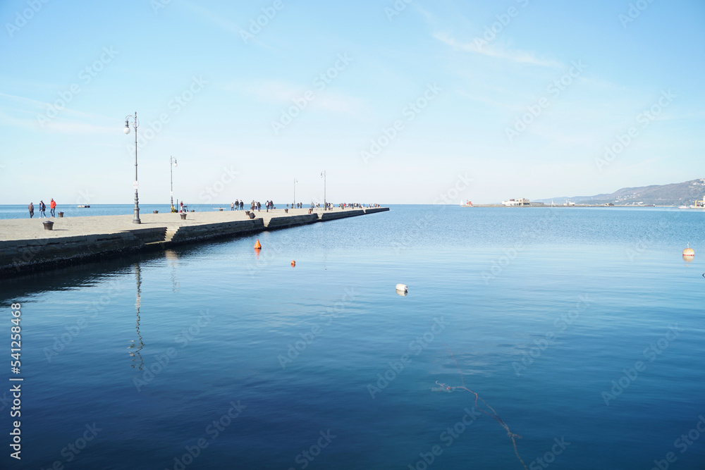 Molo presso la banchina del porto doi Trieste con cielo azzurro e mare calmo colore blu intenso - obrazy, fototapety, plakaty 