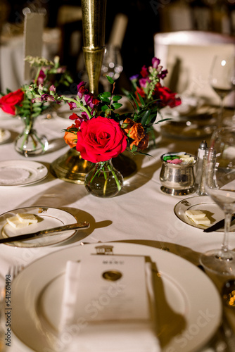 Red roses in a vase and colorful flowers on a luxury dining table. 