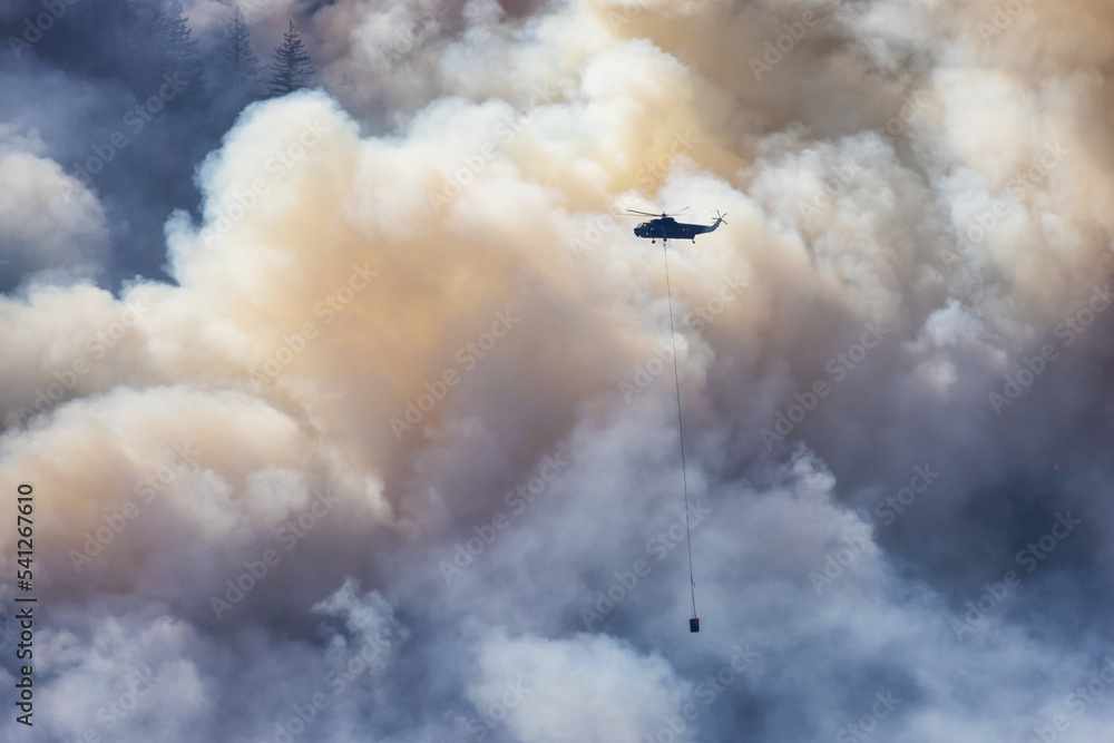 Wildfire Service Helicopter flying over BC Forest Fire and Smoke on the mountain near Hope during a hot sunny summer day. British Columbia, Canada. Natural Disaster Wildfire Service Helicopter flying over BC Forest Fire and Smoke on the mountain near Hope during a hot sunny summer day. British Columbia, Canada. Natural Disaster