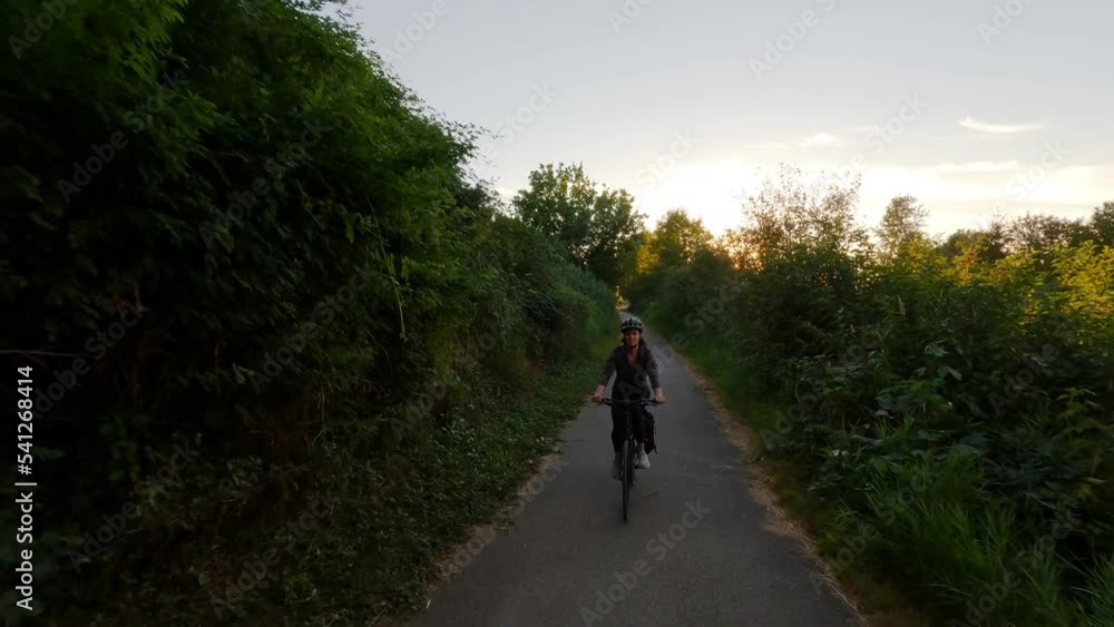 Adventure Woman bike riding on a bicycle trail surrounded by green trees. Summer Sunset. Pitt Meadows, Greater Vancouver, British Columbia, Canada. Adventure Woman bike riding on a bicycle trail surrounded by green trees. Summer Sunset. Pitt Meadows, Greater Vancouver, British Columbia, Canada.