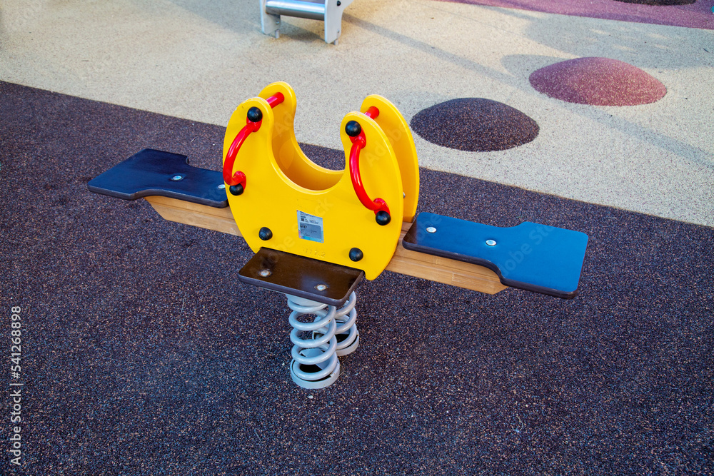 Rocking chair on a yellow and blue metal spring made of natural wood in the shape of a butterfly on a playground with a rubberized coating. Kids sports hobbies.