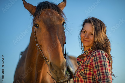 Portrait of a young beautiful girl in a field next to a horse.