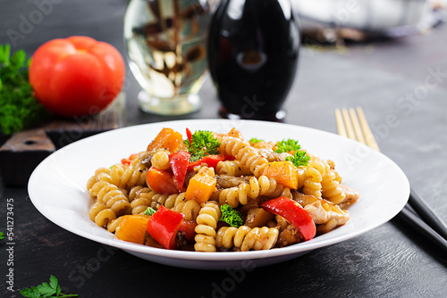 Vegetable pasta fusilli corti bucati with eggplant, sweet pepper and chicken in white plate on dark table.