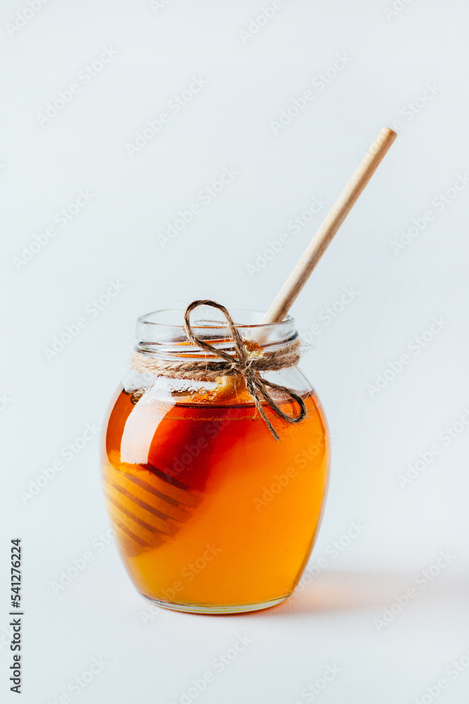close-up on a jar of honey and a wooden spindle for honey on a white background close-up on a jar of honey and a wooden spindle for honey on a white background
