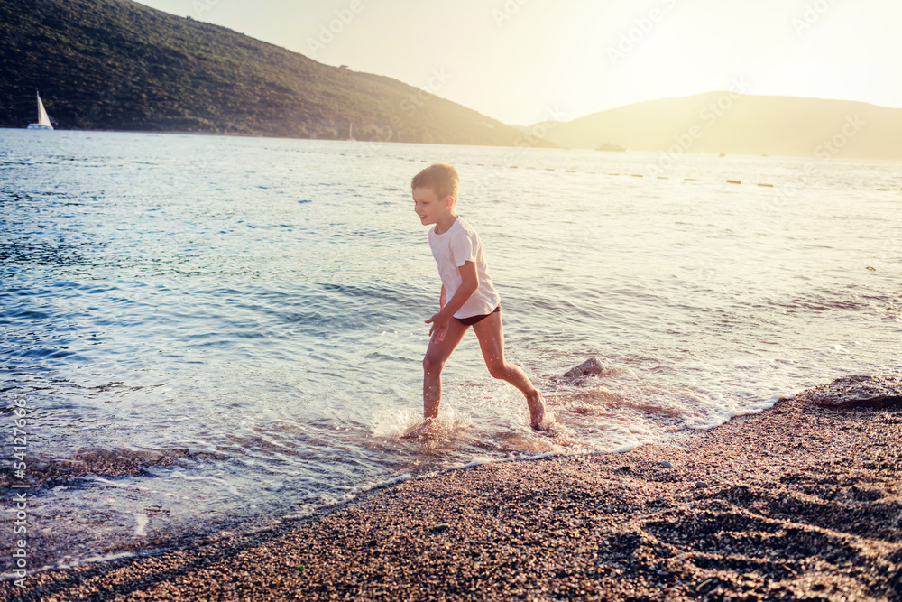 Cheerful little boy having fun while running on the beach. Happy little boy having fun while running with his arms outstretched on the beach in summer day. Copy space.