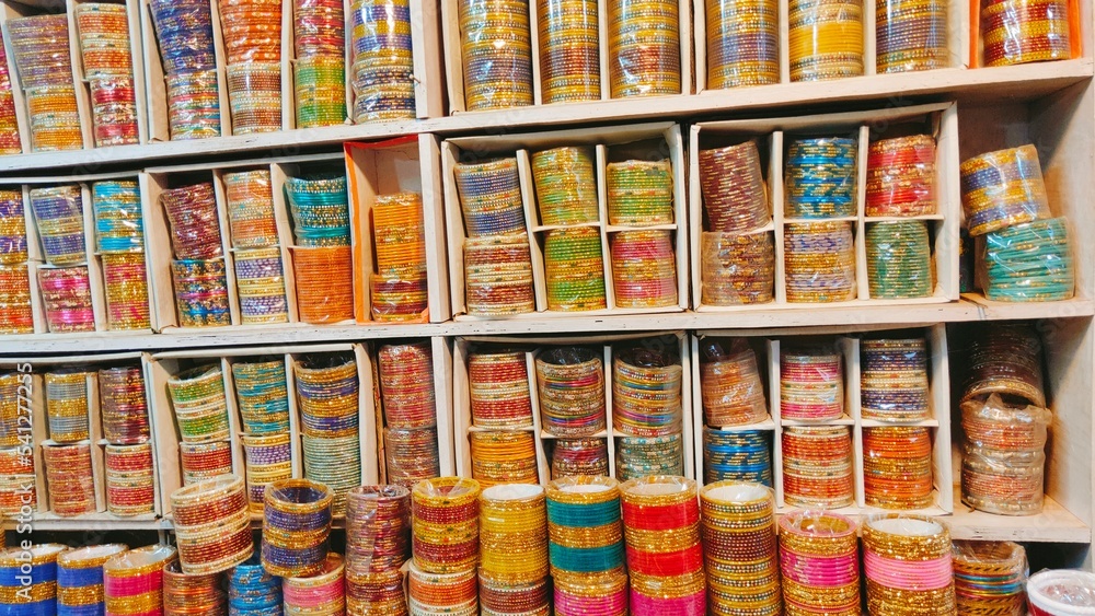 In an Indian shop, a closeup of a wide variety of bangles displayed, including those made of glass, metal, and lac, in both shiny and matte finishes,  commonly worn by females. 