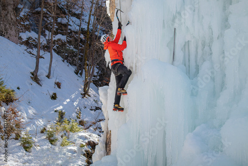 Alpinist man with ice climbing equipment on a frozen waterfall