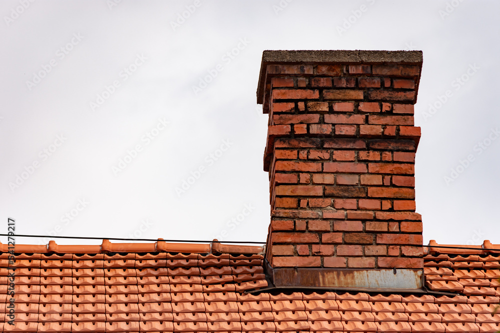 Classic chimney made of bricks on a roof with orange tiles