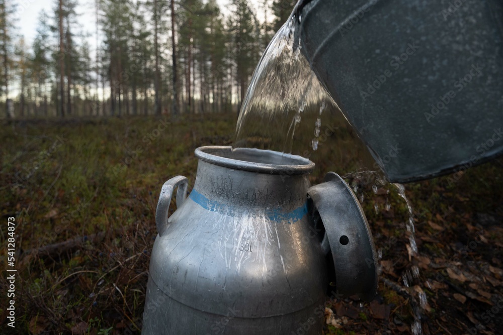 Pouring pure drinking water from bucket to old milk churn Pouring pure drinking water from bucket to old milk churn