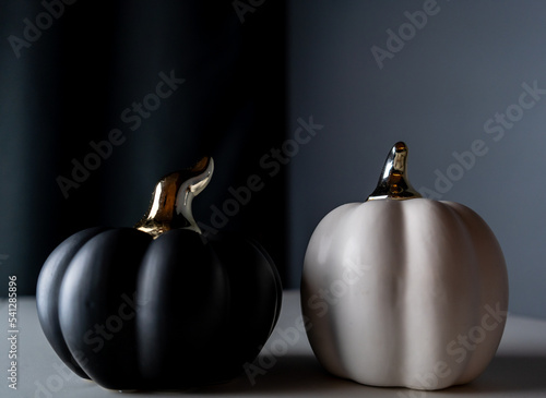 Two black and white pumpkins with white one on the right and black on the left side. Stylish halloween decoration for spooky party. Pumpkins in two colours on three shades of grey split background.
