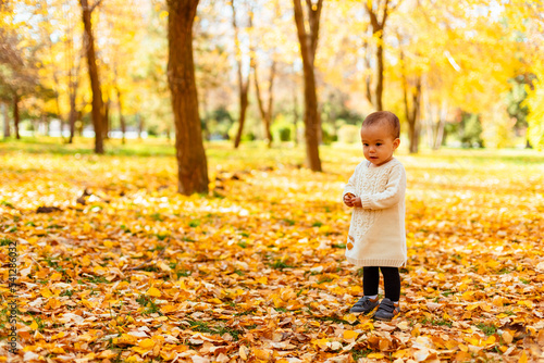 Toddler standing in yellow leaves in autumn park