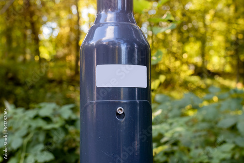 Close up of a blank white sticker on metallic light post with forest in the background