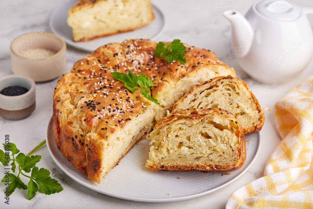 Savory layered pie from yeast dough with mozzarella and feta cheese, parsley and sesame seeds.