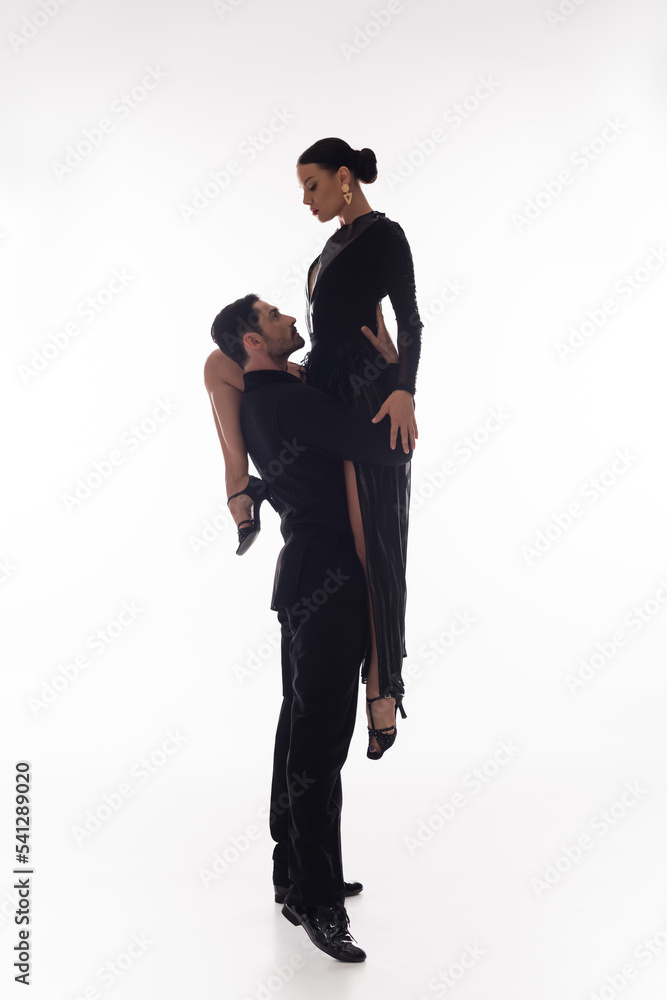 Side view of man in suit lifting partner in dress on white background Side view of man in suit lifting partner in dress on white background