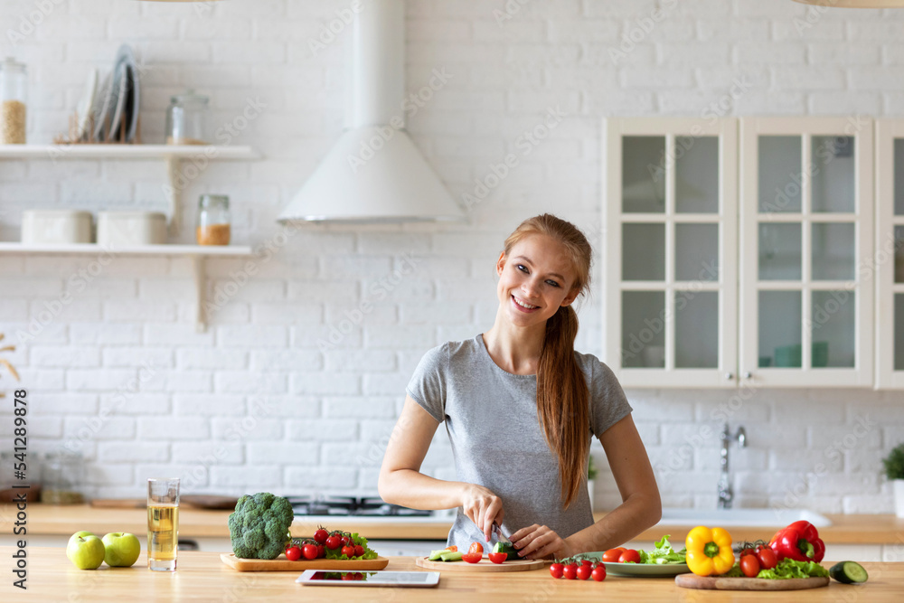 Young funny woman preparing vegetable salad in kitchen at home.