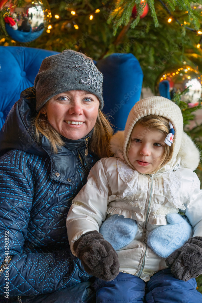 Obraz premium Happy Mother Holding Cute Baby Girl in Warm Clothes Against Christmas Tree Outdoors