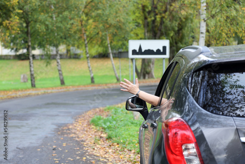 Dłoń kobiety, ręka wysunięta przez okno samochodu osobowego, suwa, na drodze, znak obszar zabudowany.
