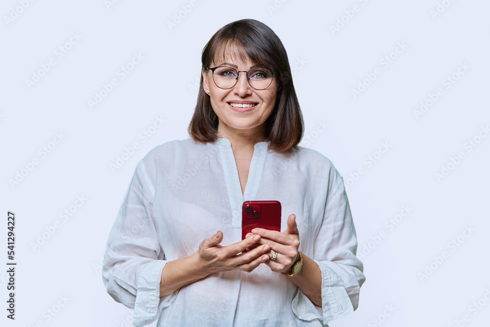 Portrait of middle aged woman with phone looking at camera on white background Portrait of middle aged woman with phone looking at camera on white background