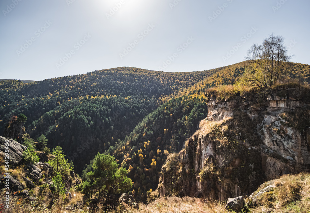 Mountains and hills overgrown with dense forest in autumn, rocky cliffs in the mountains, on a sunny day in the Caucasus
