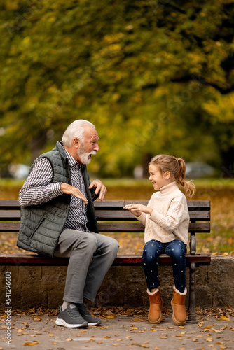 Grandfather playing red hands slapping game with his granddaughter in park on autumn day