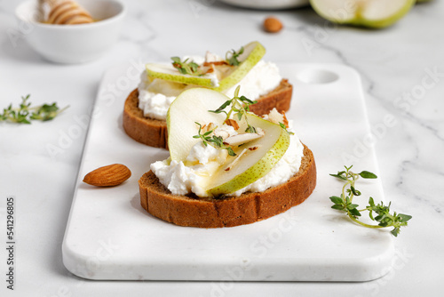 Bread toast with ricotta cheese, cream cheese, honey, pear, thyme on white board and marble table. Snack, bruschetta. Close up. photo