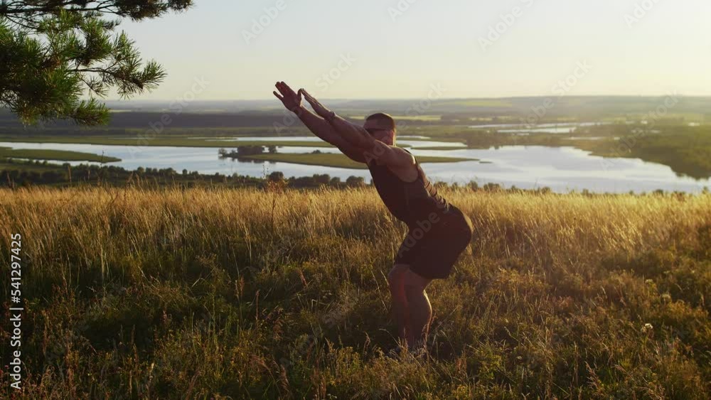 A muscular man wearing sportswear and sunglasses warming up on the hill at sunset A muscular man wearing sportswear and sunglasses warming up on the hill at sunset